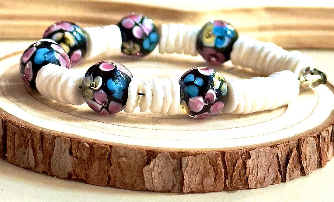 Side view of Moonlit Garden bracelet on a wood slice, showing colorful flowers on black beads between white disc beads.