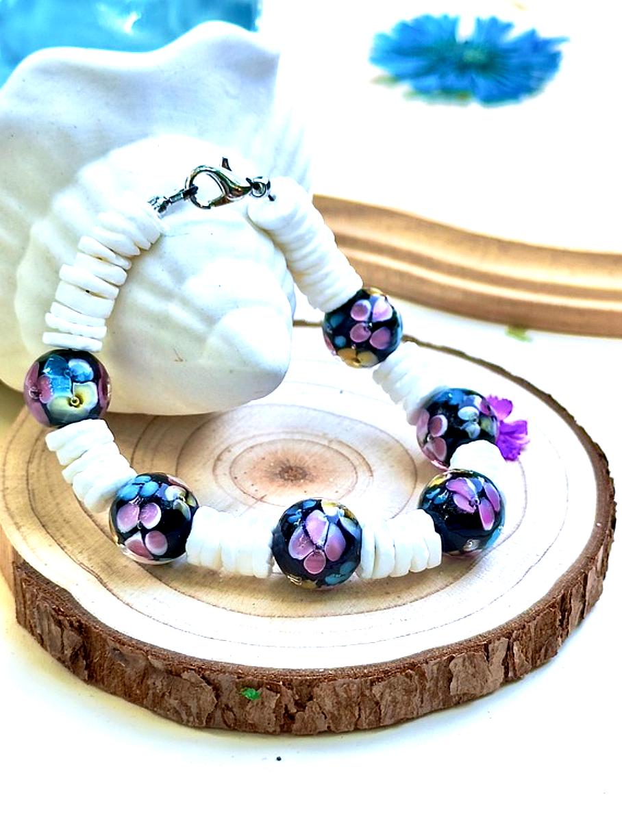 Moonlit Garden floral bracelet displayed on a wood slice with seashells and blue floral accents.