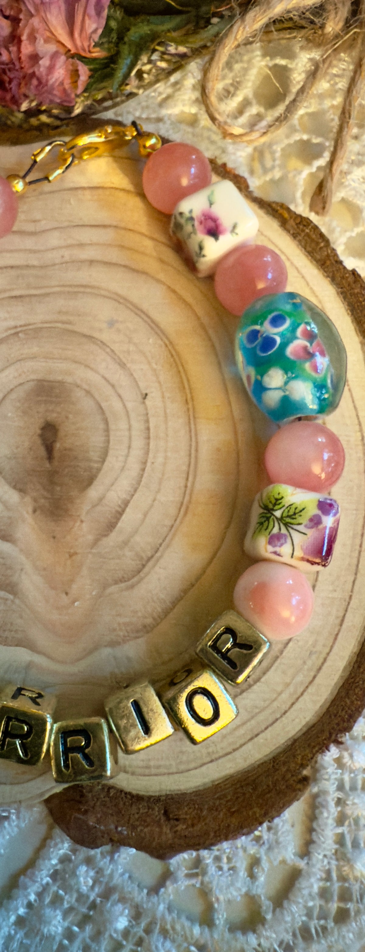 Close-up of a breast cancer awareness bracelet with colorful beads and the word 'WARRIOR' on a wooden background.