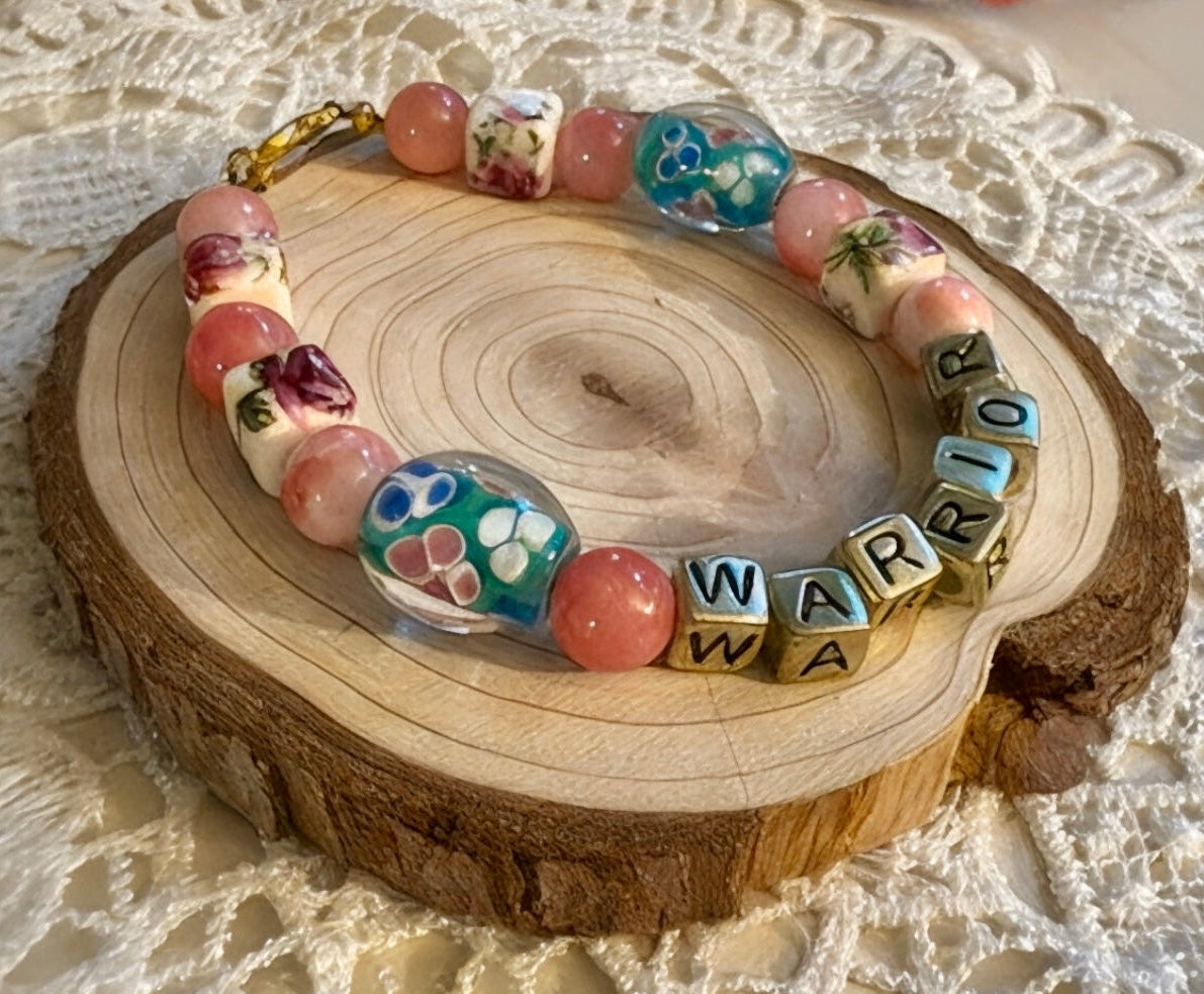 Breast cancer awareness bracelet featuring colorful beads and letters spelling 'WARRIOR', symbolizing strength and support.