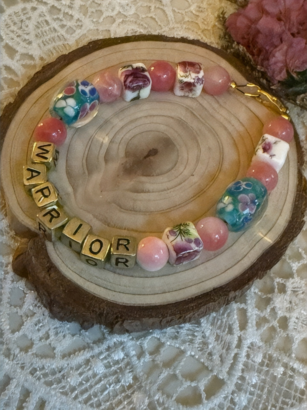 Breast cancer awareness bracelet featuring colorful beads and 'WARRIOR' letters on a wooden display.