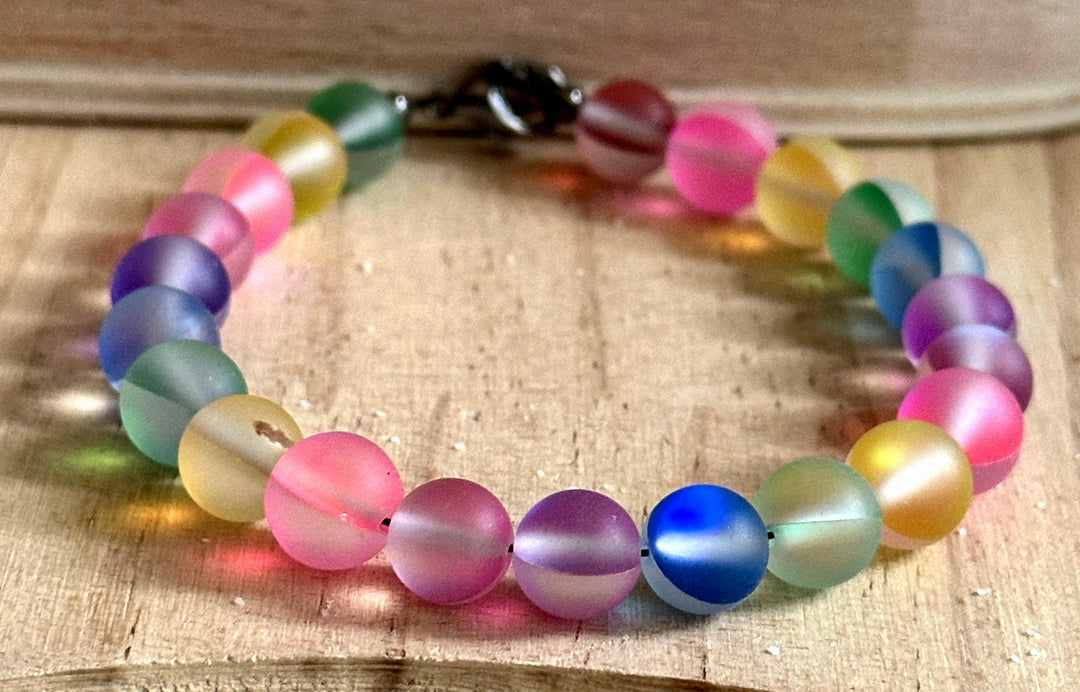 Handmade rainbow bracelet photographed on natural wood showing colorful frosted glass beads and lobster clasp closure.