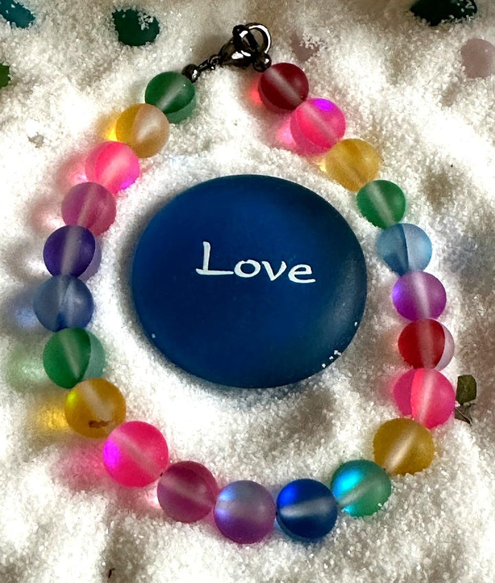 Rainbow Connection bracelet displayed beside a blue Love stone representing acceptance, connection, and Pride.