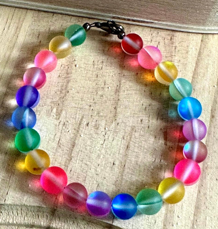 Colorful rainbow beaded Pride bracelet displayed on natural wood showcasing vibrant frosted glass beads.