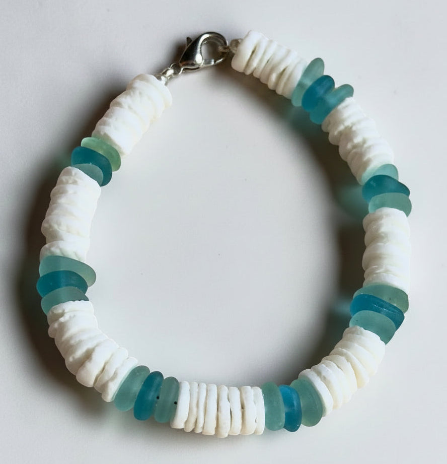 Handmade coastal bracelet with white shell beads and aqua sea glass inspired accents styled on neutral stone with soft beach decor