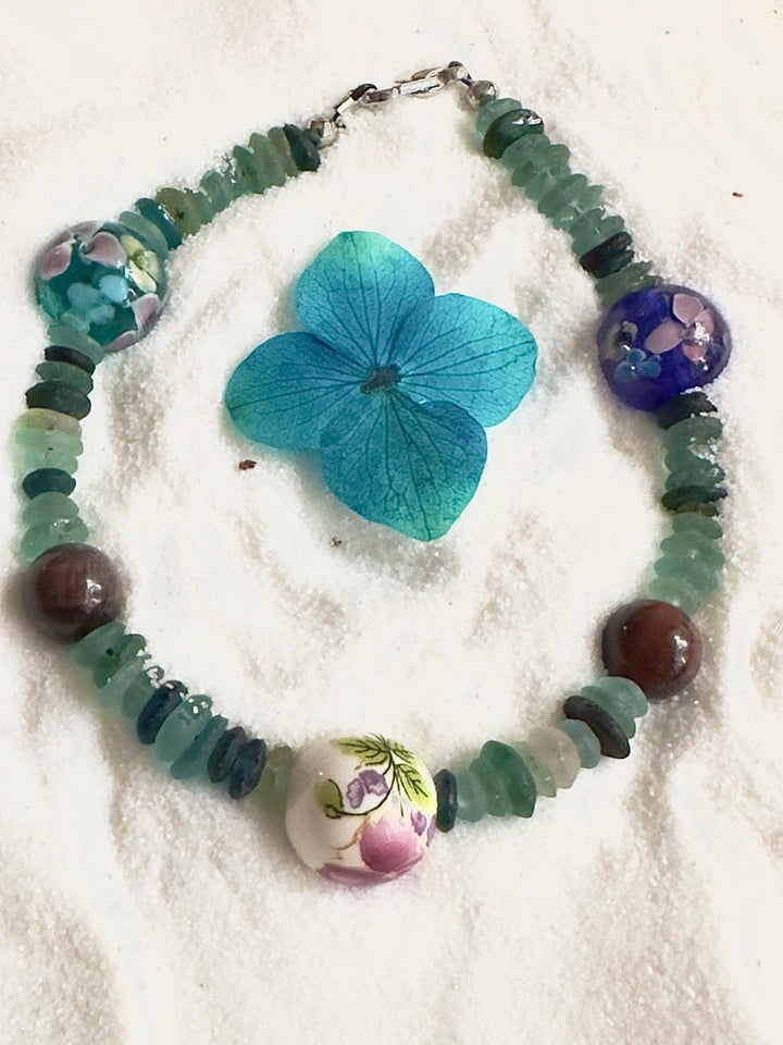 Green sea glass bead bracelet with floral centerpiece on neutral background