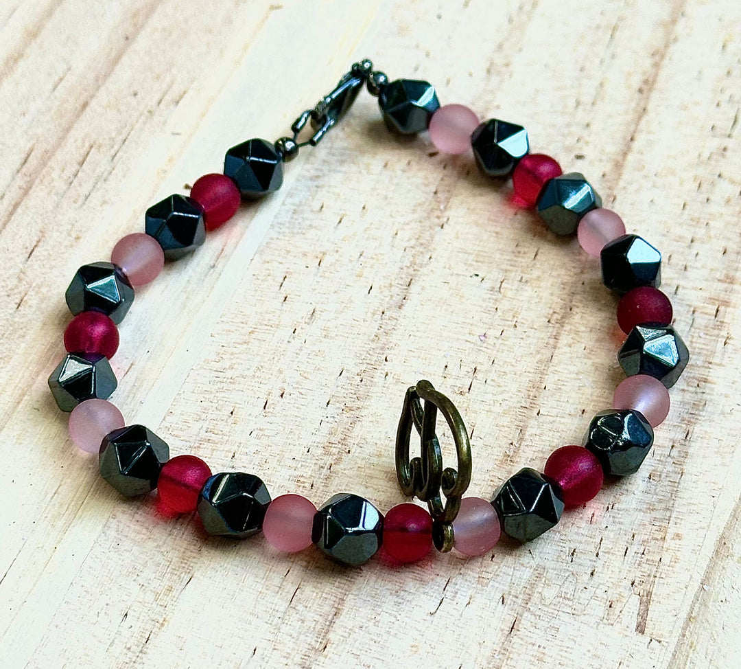 Flat lay of the Soul Connection bracelet showcasing pink, raspberry, black, and hematite beads with an intertwined heart charm.