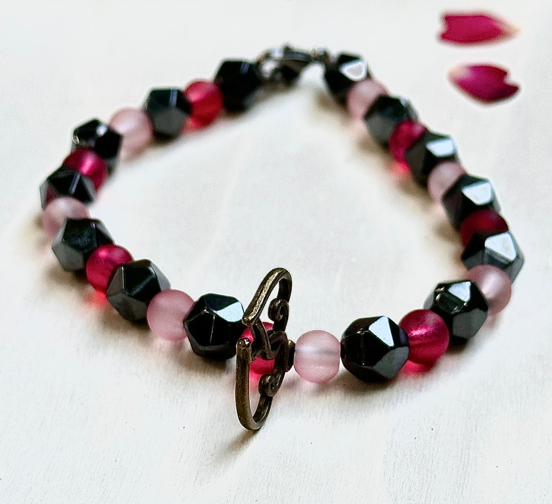 Beaded bracelet with pink and black beads on a white surface with rose petals.