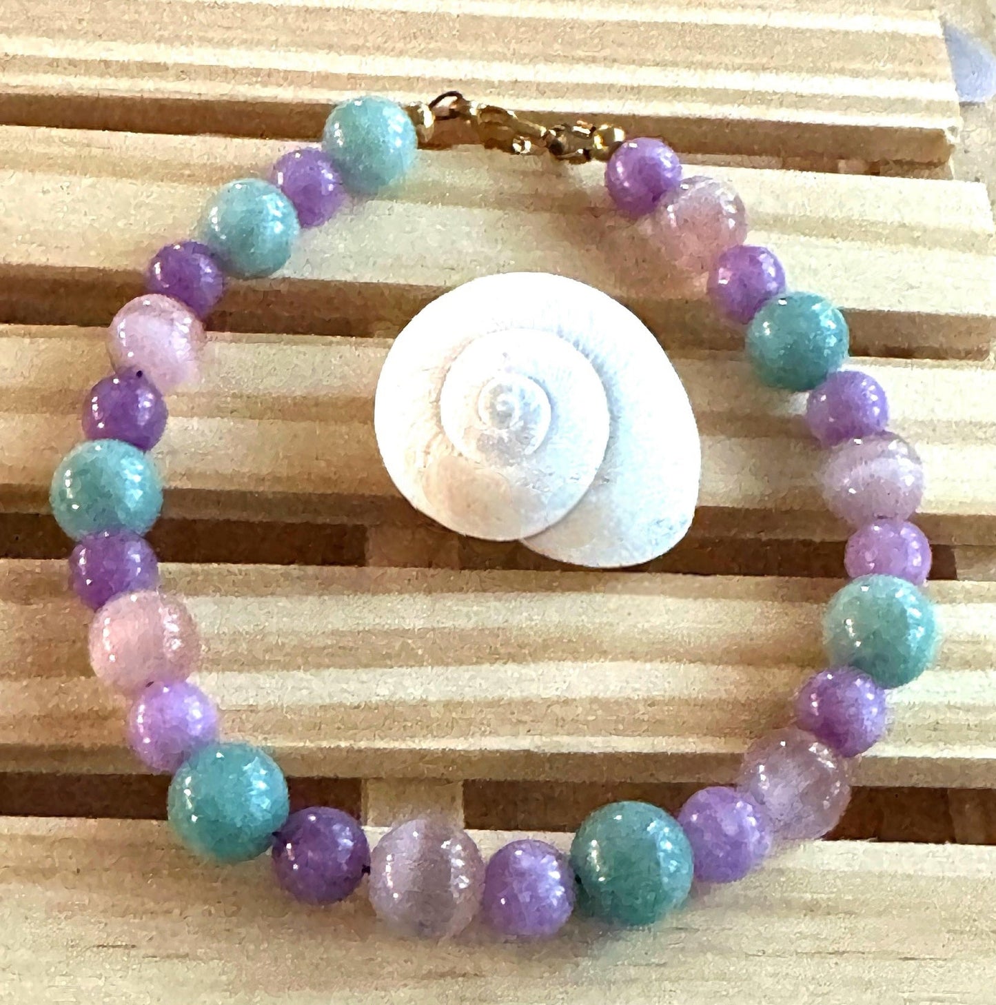 Pastel Spring Garden Serenity bracelet arranged beside a seashell on a wooden platform.