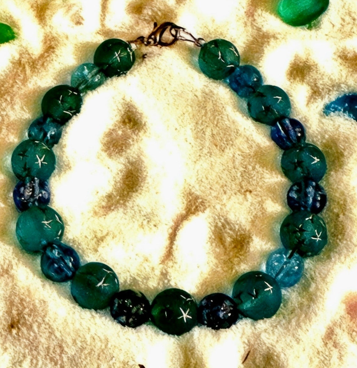 Aqua-blue celestial bracelet with star-pattern beads displayed on a sandy beach-inspired background.