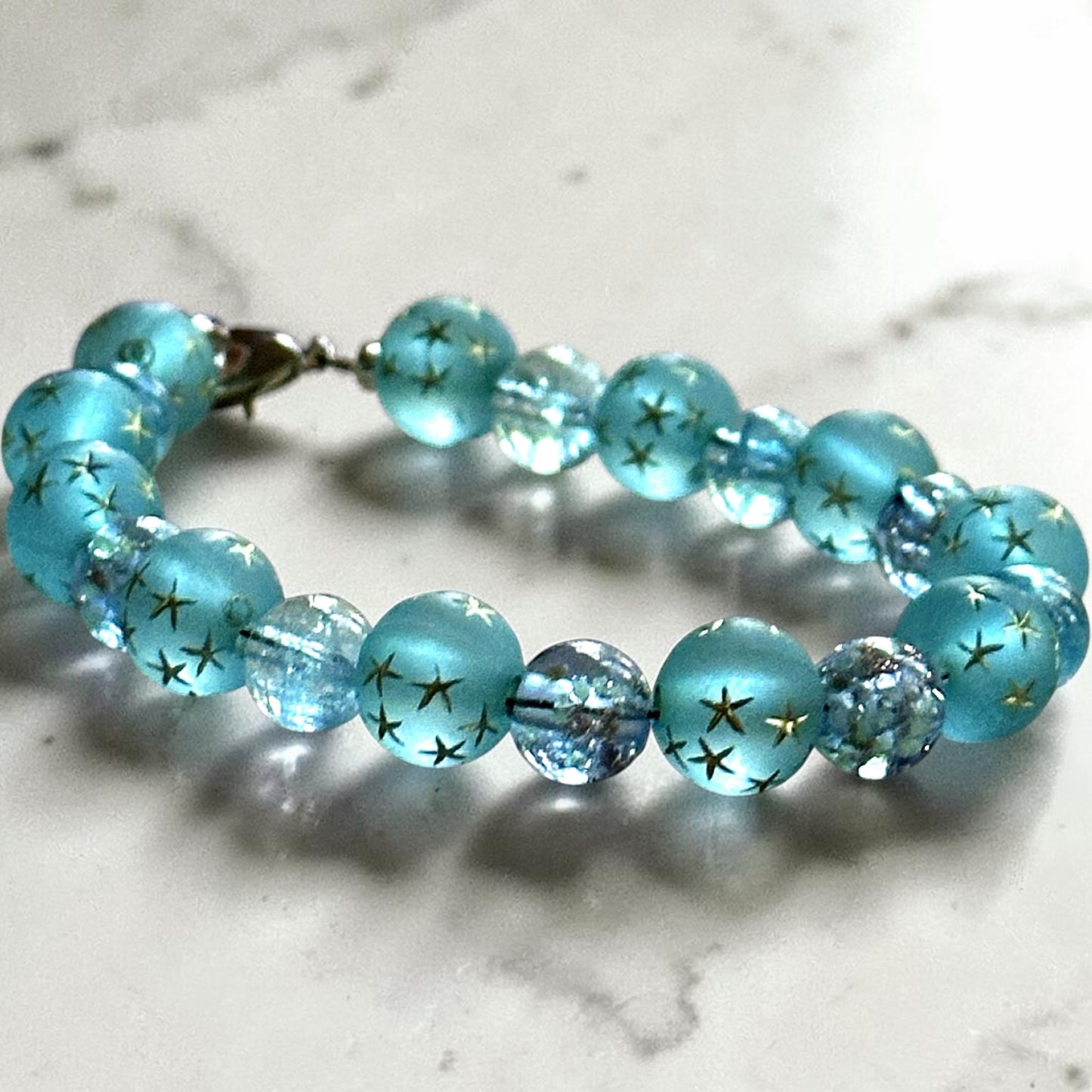 Handmade Starfall Constellations bracelet resting on a marble surface showcasing frosted blue star beads and sparkling crystal details.