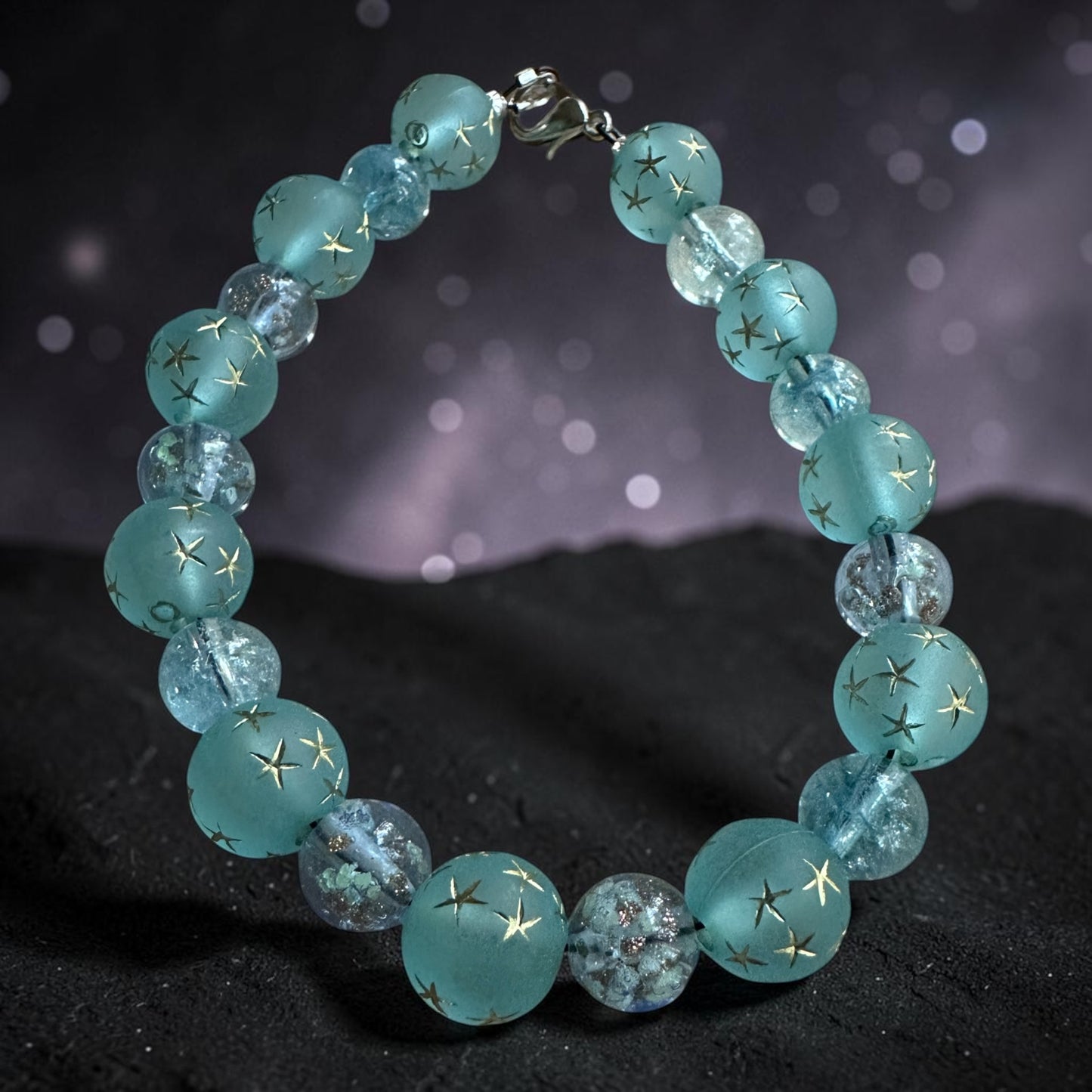 Celestial-inspired bracelet with aqua-blue star beads photographed against a dreamy purple night sky background.