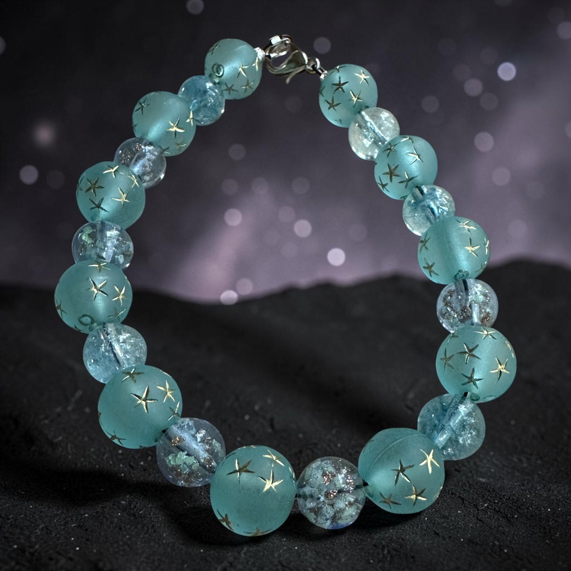 Celestial-inspired bracelet with aqua-blue star beads photographed against a dreamy purple night sky background.