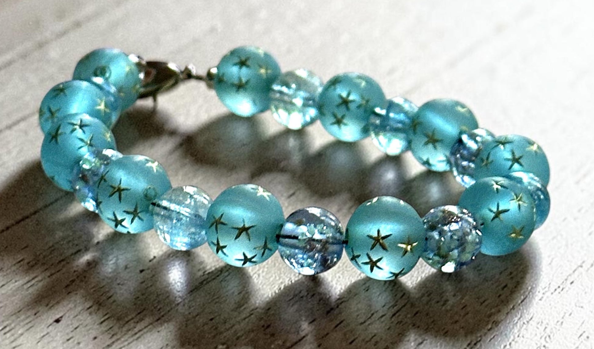 Close-up of frosted aqua-blue glass beads with gold star details and sparkling crystal accents in the Starfall Constellations bracelet.