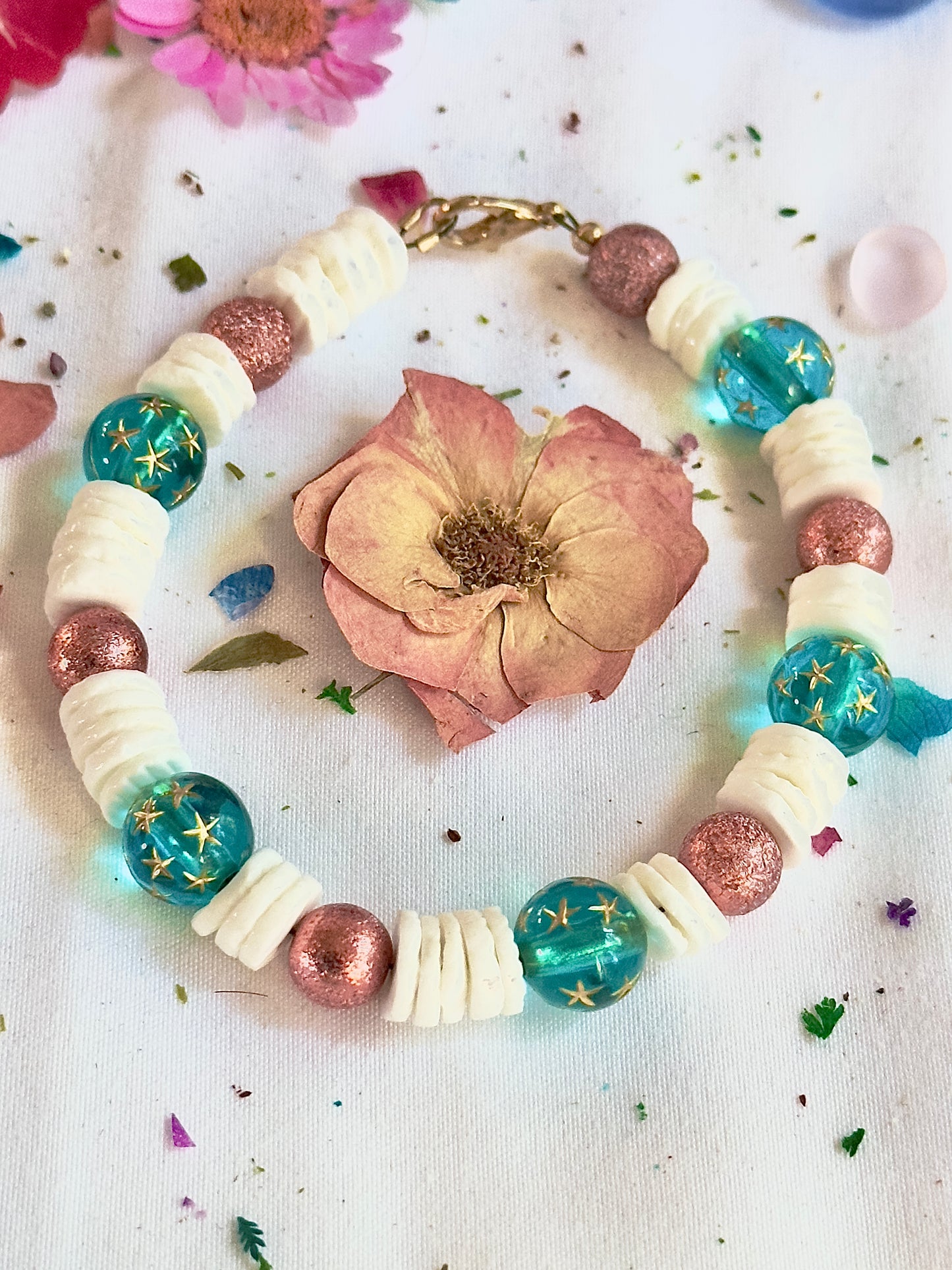 Celestial coastal bracelet styled with flowers and soft pastel accents in dreamy flat lay photography