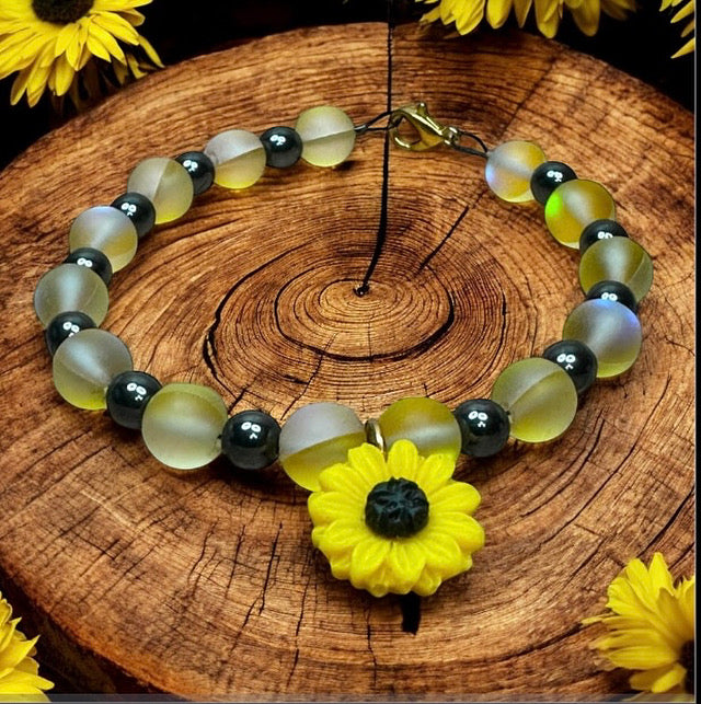 Nature-inspired Sunflower Anchor bracelet displayed on a rustic wood slice surrounded by sunflowers, highlighting frosted yellow and black beads.