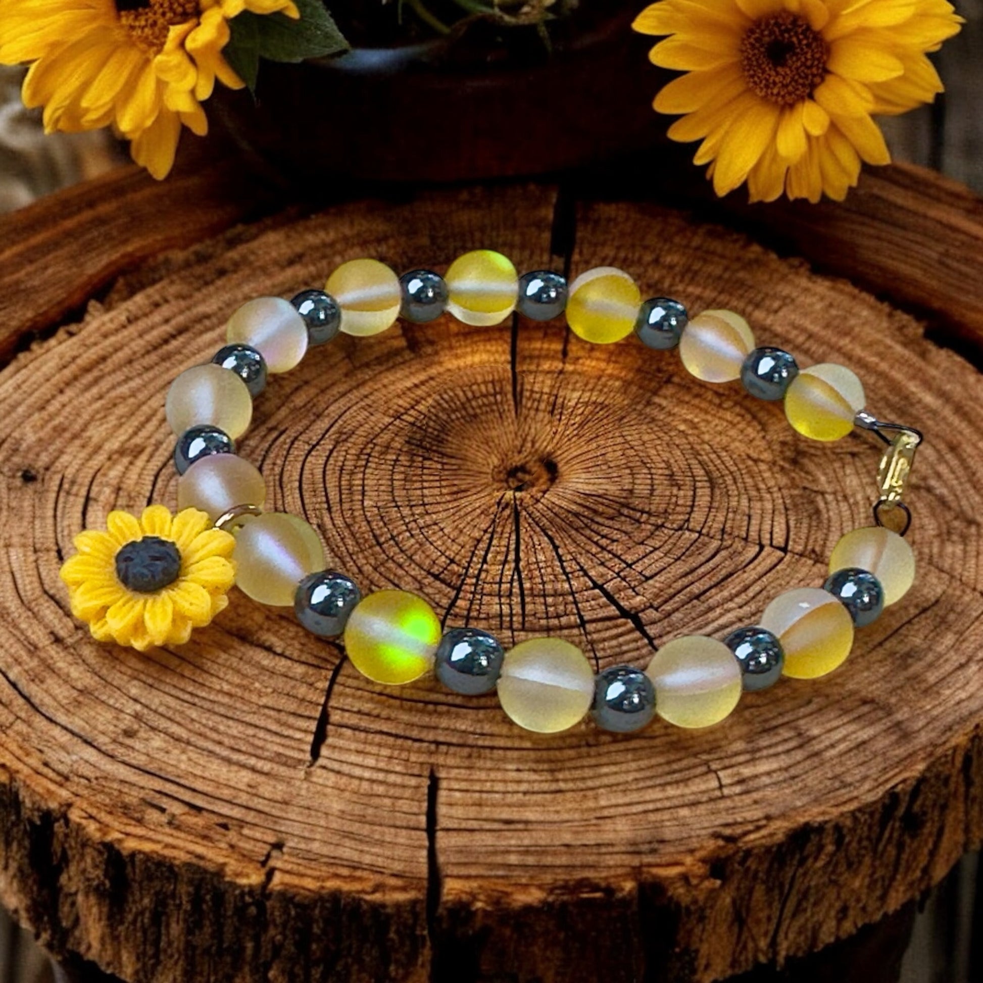 Close-up of Sunflower Anchor bracelet on a rustic wood surface with sunflowers, showcasing frosted yellow beads, iridescent accents, and clay sunflower charm.