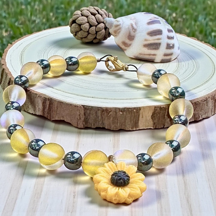 Handmade Sunflower Anchor bracelet displayed on a natural wood slice with a seashell, featuring frosted yellow beads, black accents, and a clay sunflower focal charm.