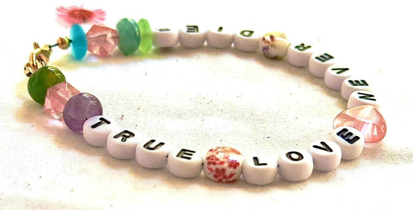 Angled view of the True Love Never Dies bracelet showing pastel beads, floral accents, heart centerpiece, and gold clasp.