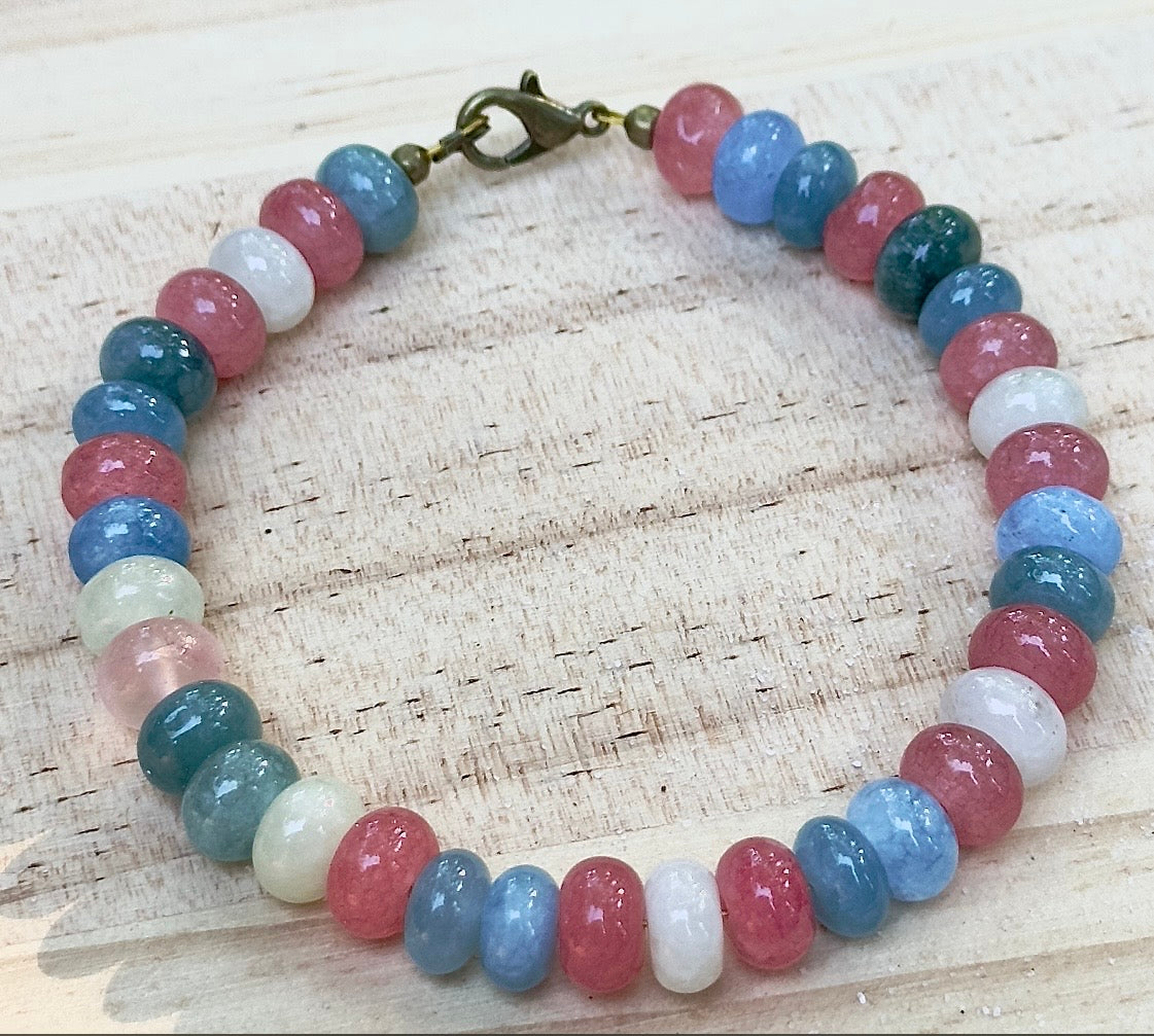 Trans Pride inspired bracelet with pink, white, and blue beads displayed on a light wood background.
