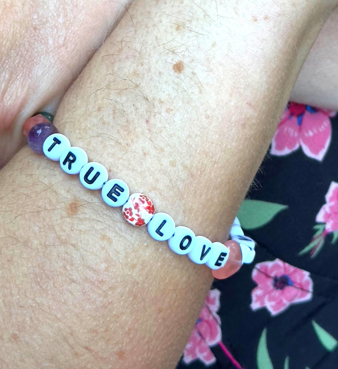 Person wearing the True Love Never Dies bracelet on their wrist, displaying the heartfelt message and colorful bead details.