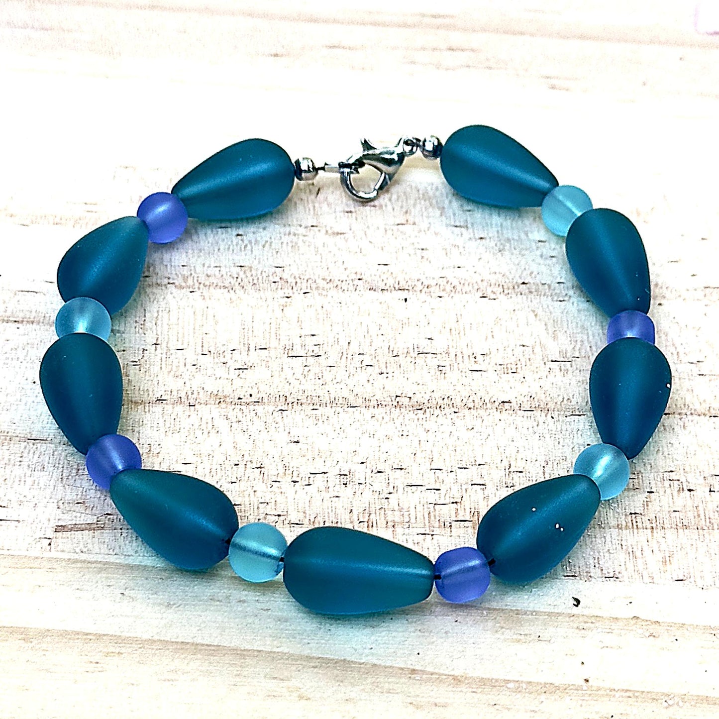 Blue and teal ocean inspired bracelet with frosted beads on light natural wood background