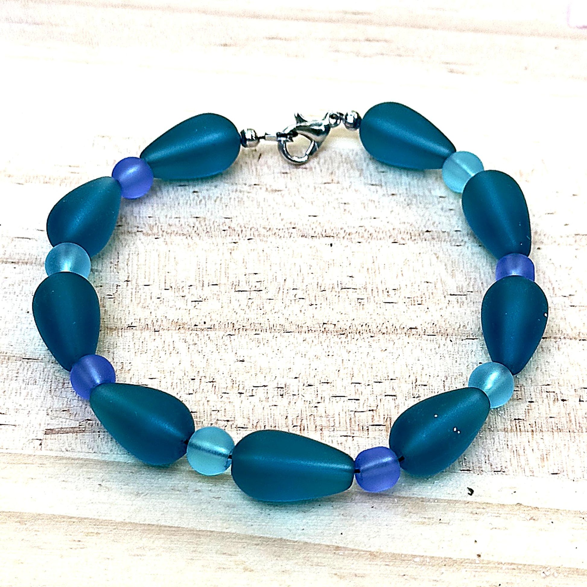 Blue and teal ocean inspired bracelet with frosted beads on light natural wood background