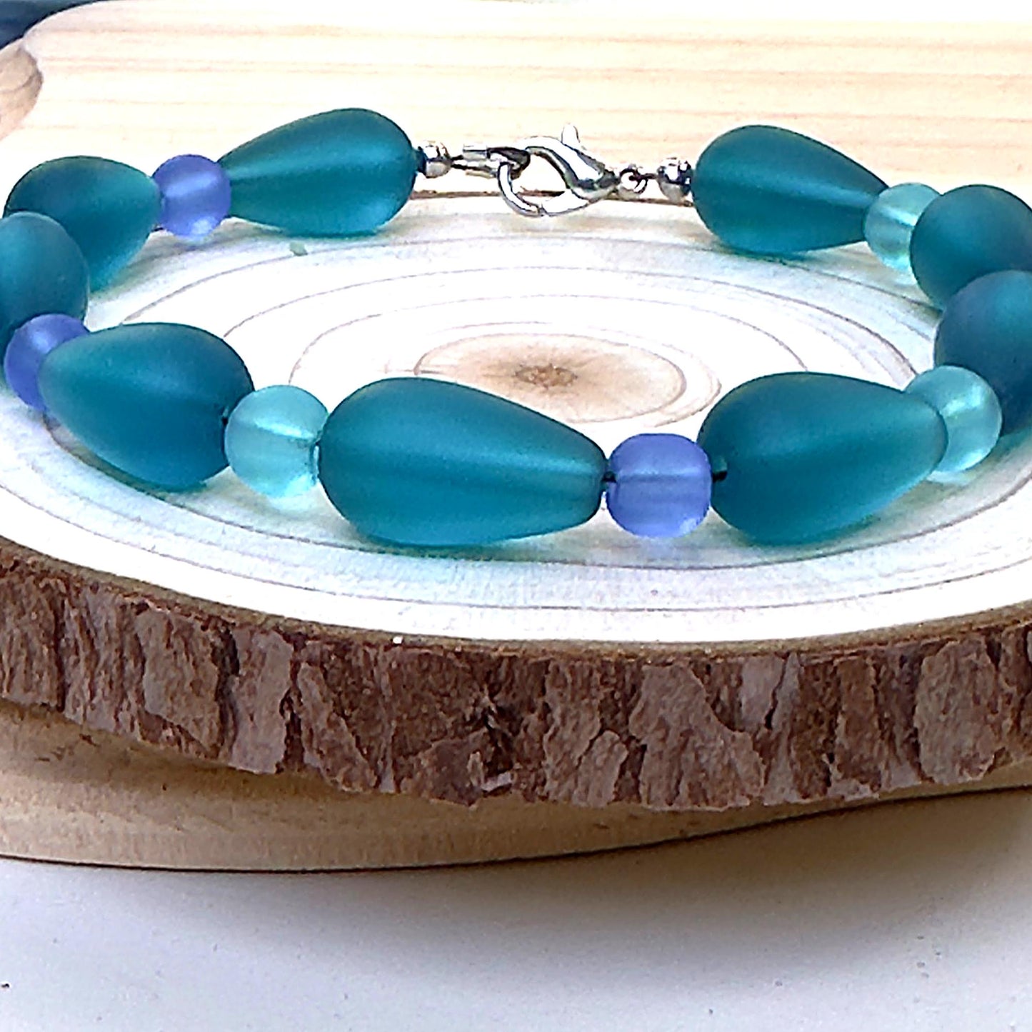 Twilight Waterfalls bracelet displayed on rustic wood slice with teal and blue glass beads