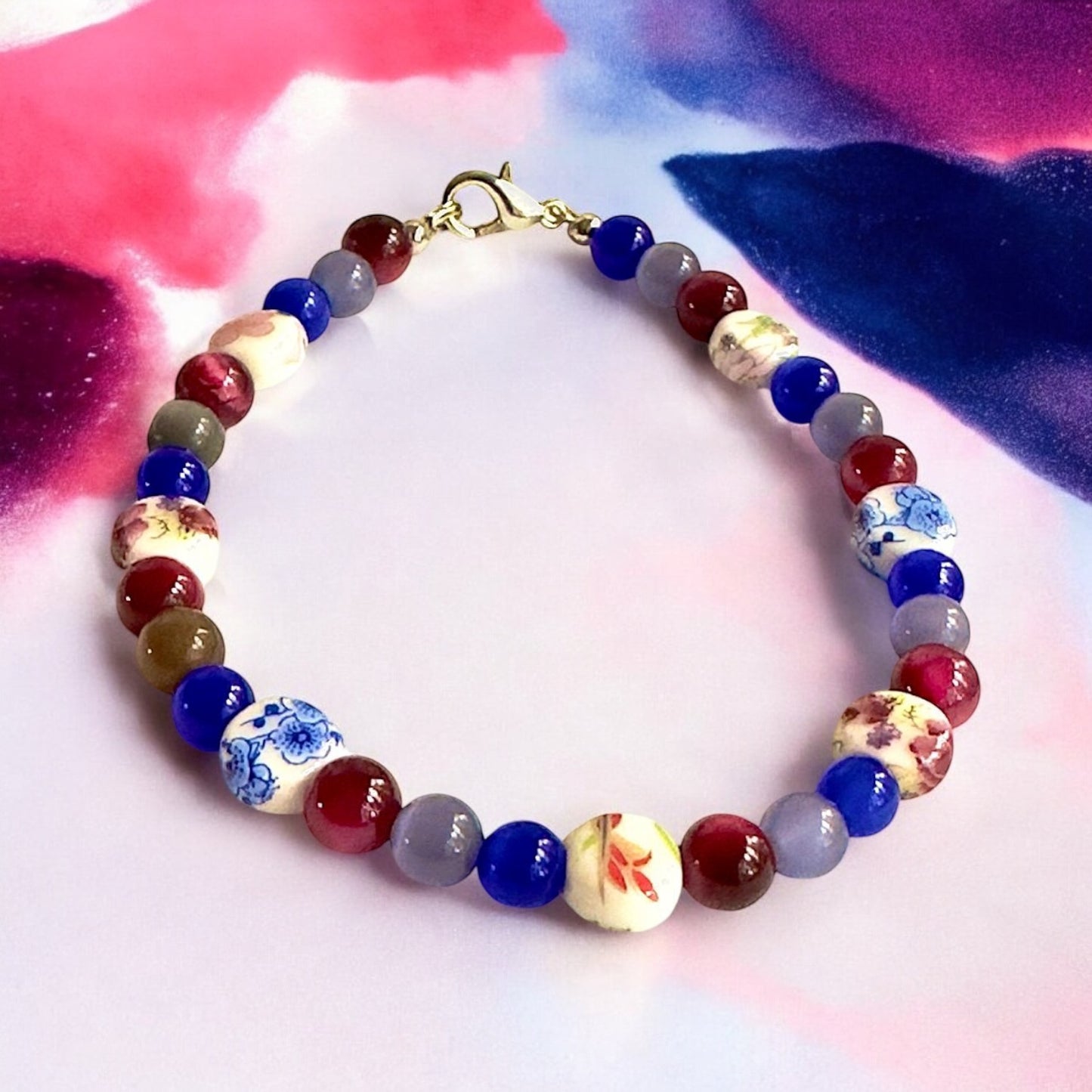     Colorful bisexual Pride inspired beaded bracelet styled on a soft pink and purple artistic background.