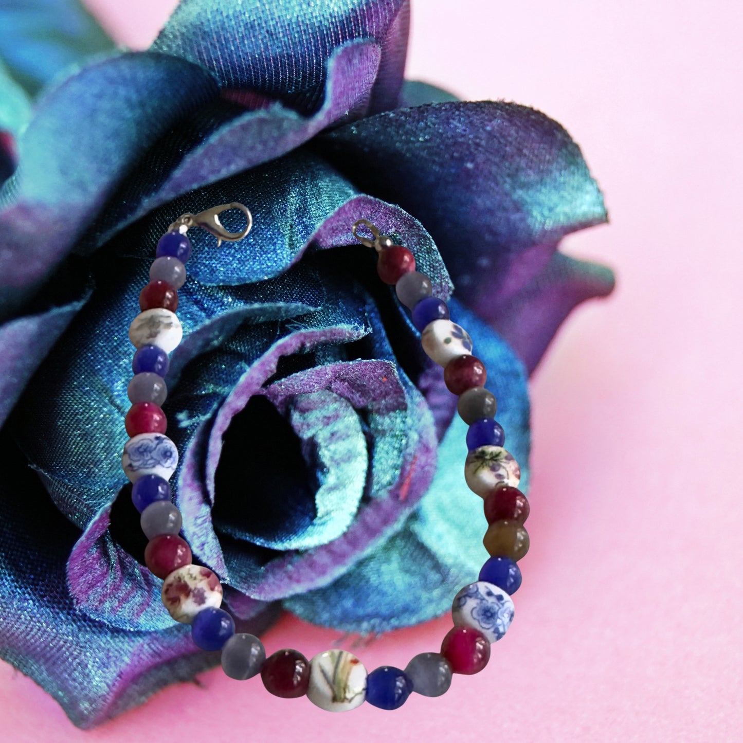     Handmade Pride bracelet displayed inside a blue and purple rose with dreamy floral styling and vibrant gemstone colors.