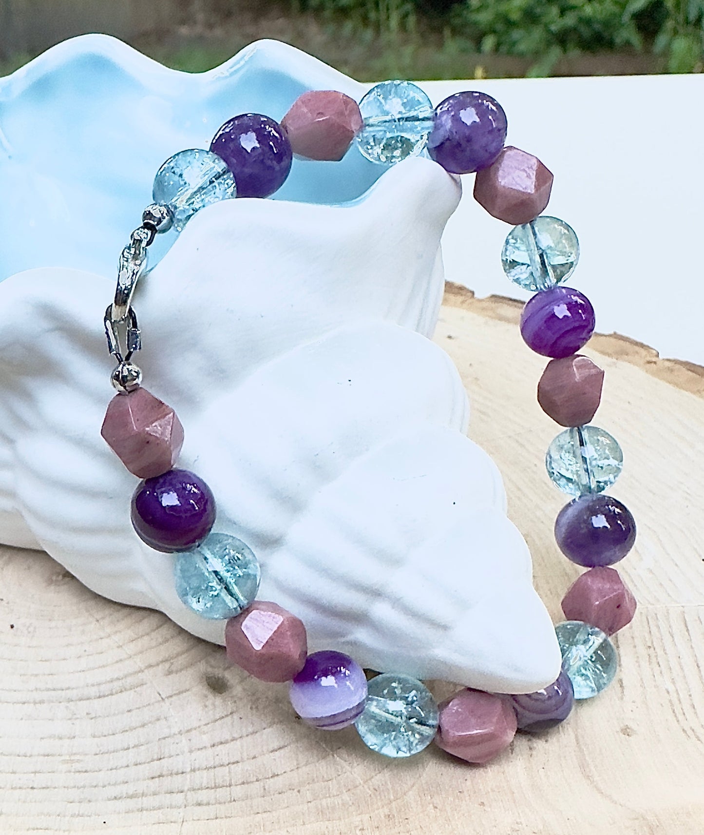 Celestial gemstone bracelet with purple and aqua beads displayed around white seashell