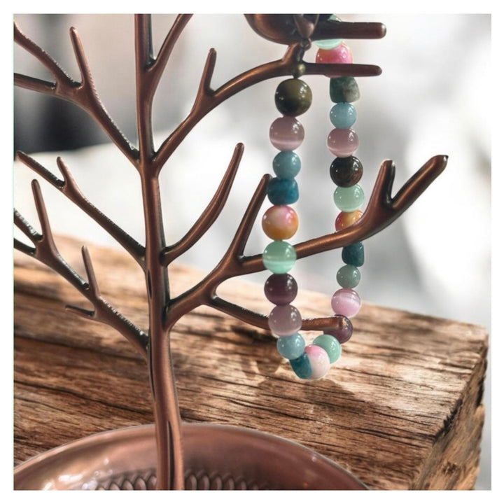 Earth and Sea gemstone bracelet hanging from a rustic wooden jewelry tree, showing its mix of teal, aqua, pink, purple and earthy-toned beads.