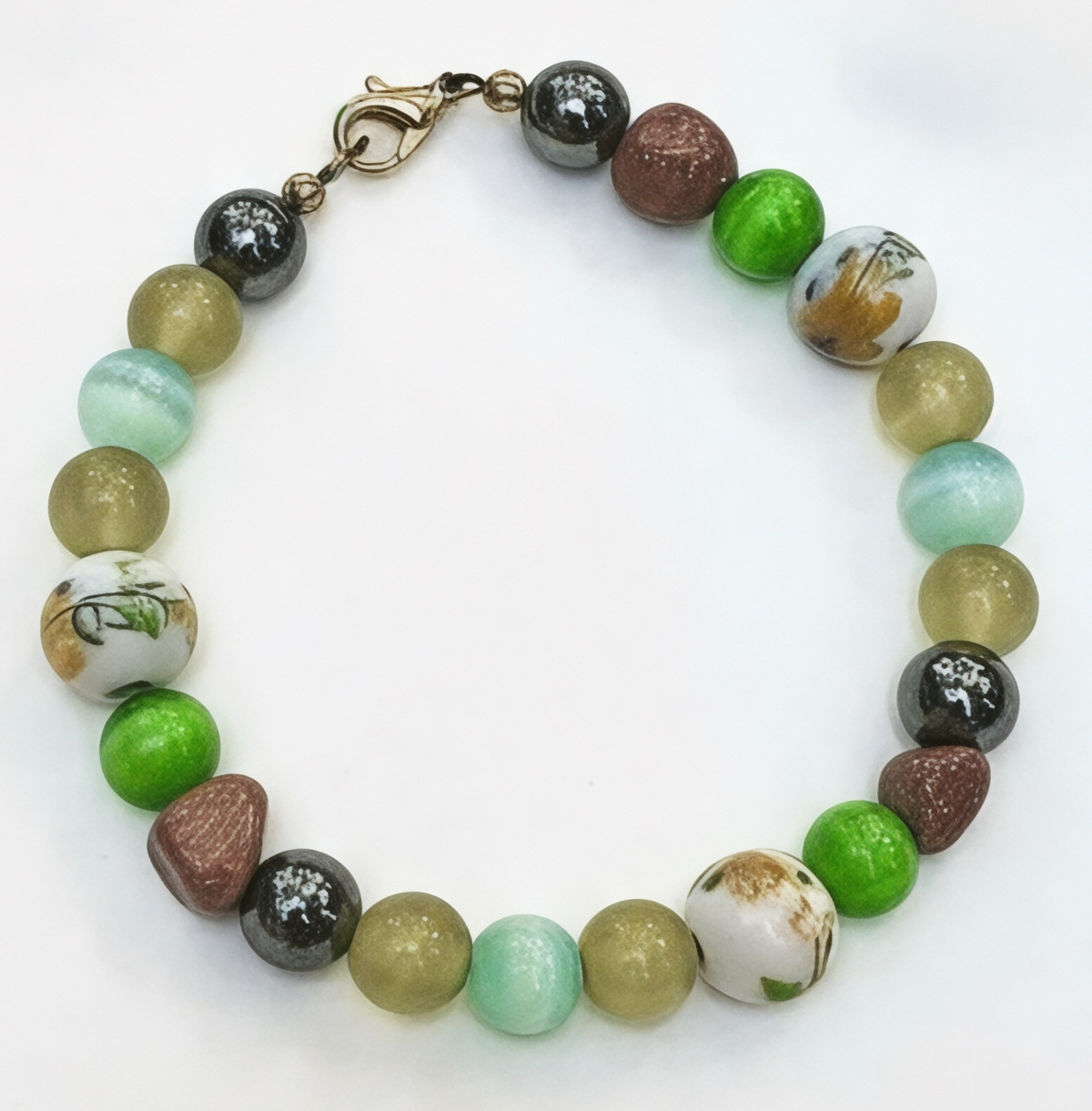 Willow Garden handmade floral bracelet displayed on a white background, featuring soft aqua, green, golden yellow, sparkling brown, and dark metallic beads with floral accents and a lobster clasp.
