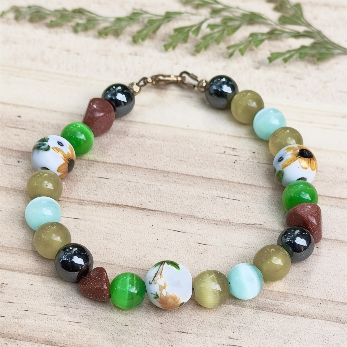 Willow Garden bracelet photographed on pale wooden planks, highlighting its delicate floral beads, aqua and green accents, sparkling brown beads, and dark metallic details.