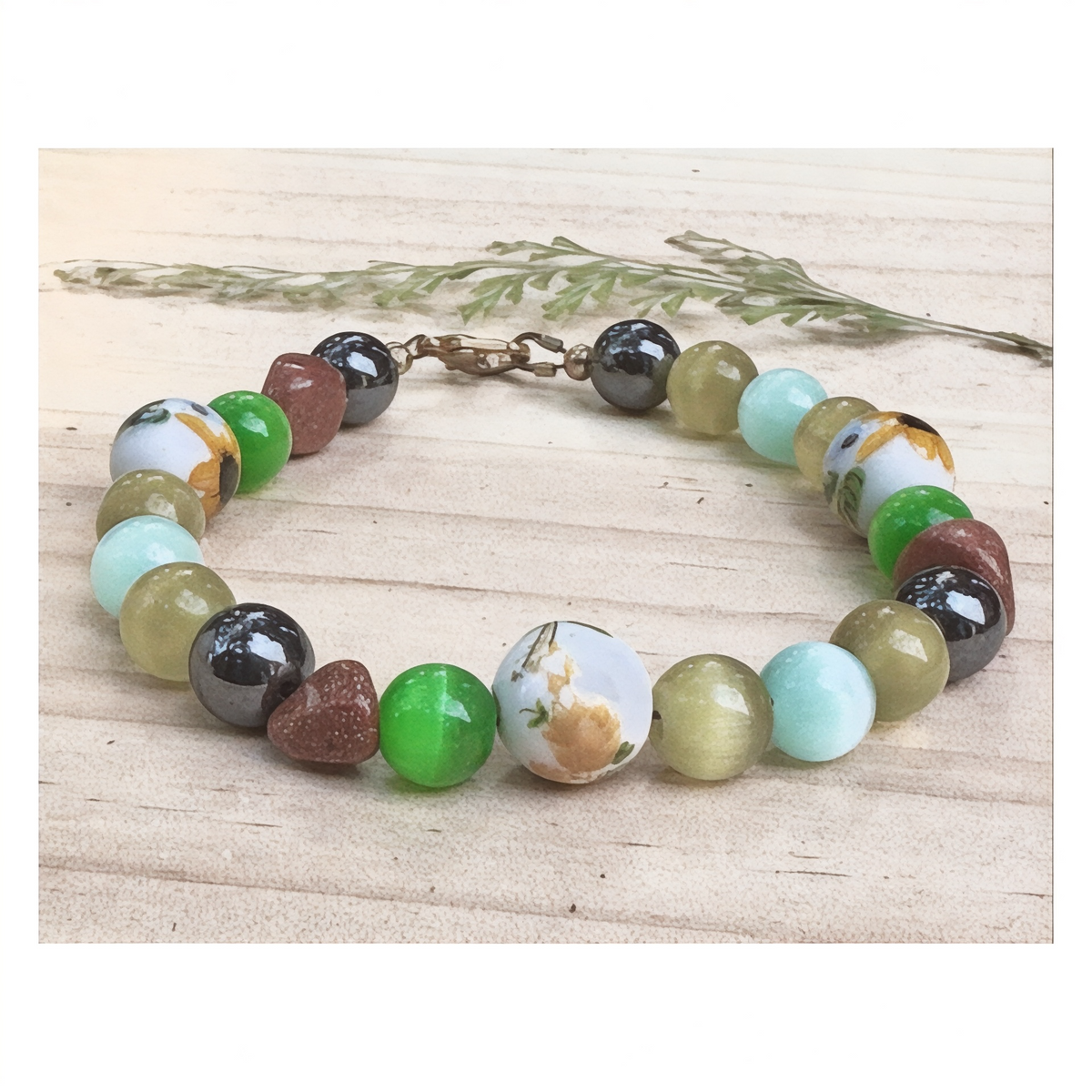 Willow Garden floral beaded bracelet resting on light rustic wood with greenery, showcasing colorful botanical-inspired beads and a gold-tone clasp.