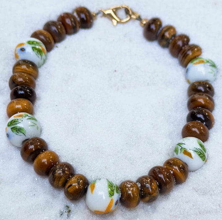 Tigers Eye and Sunflower porcelain beaded bracelet laying on sand as neutral background