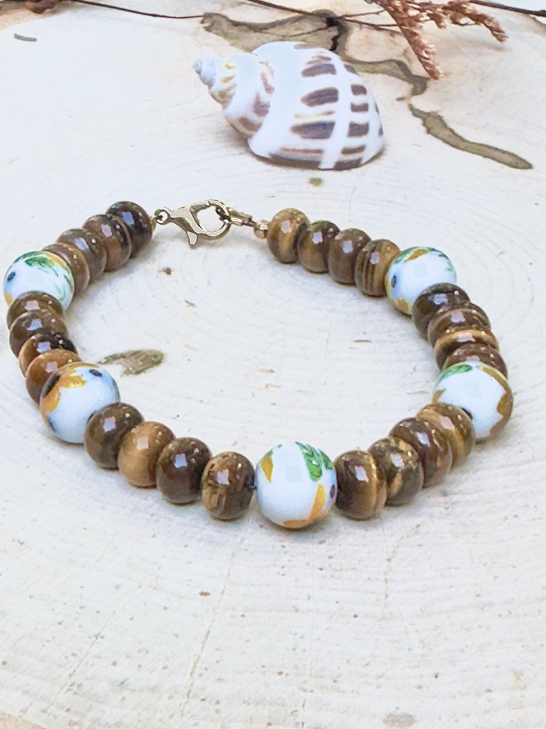Beaded bracelet with ceramic beads on a textured surface with a shell in the background