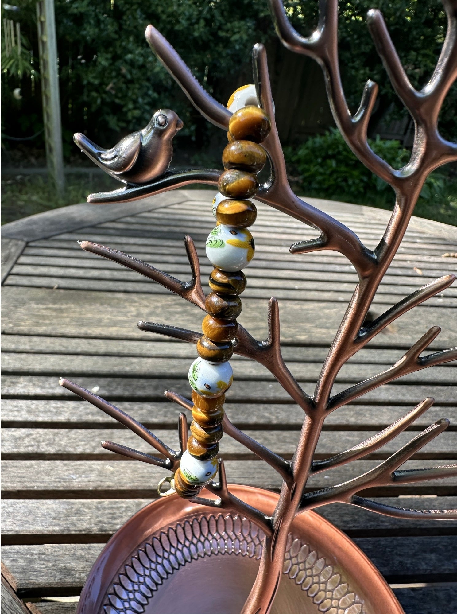 Decorative metal piece with beads and a bird on a wooden surface