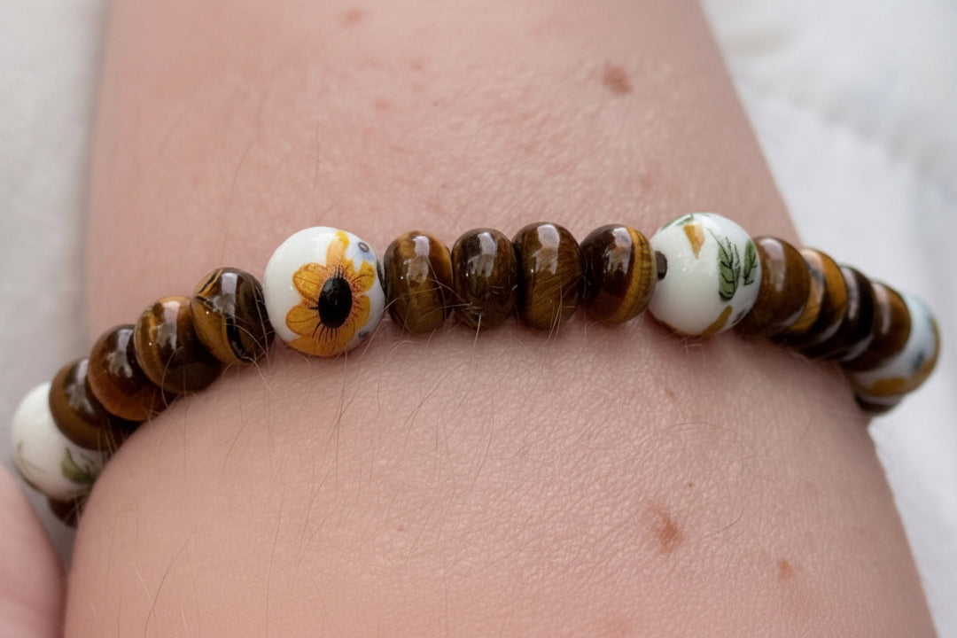 Tiger eye gemstone beaded bracelet with sunflower ceramic bead worn on wrist, handmade nature inspired jewelry