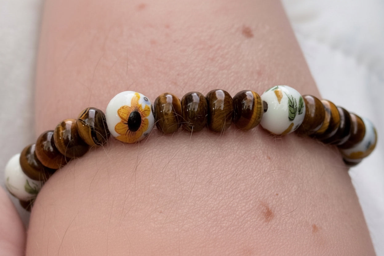Tiger eye gemstone beaded bracelet with sunflower ceramic bead worn on wrist, handmade nature inspired jewelry