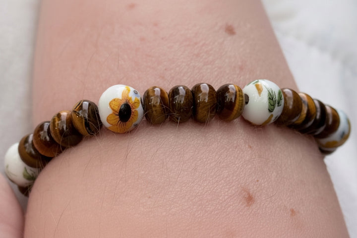 Tiger eye gemstone beaded bracelet with sunflower ceramic bead worn on wrist, handmade nature inspired jewelry
