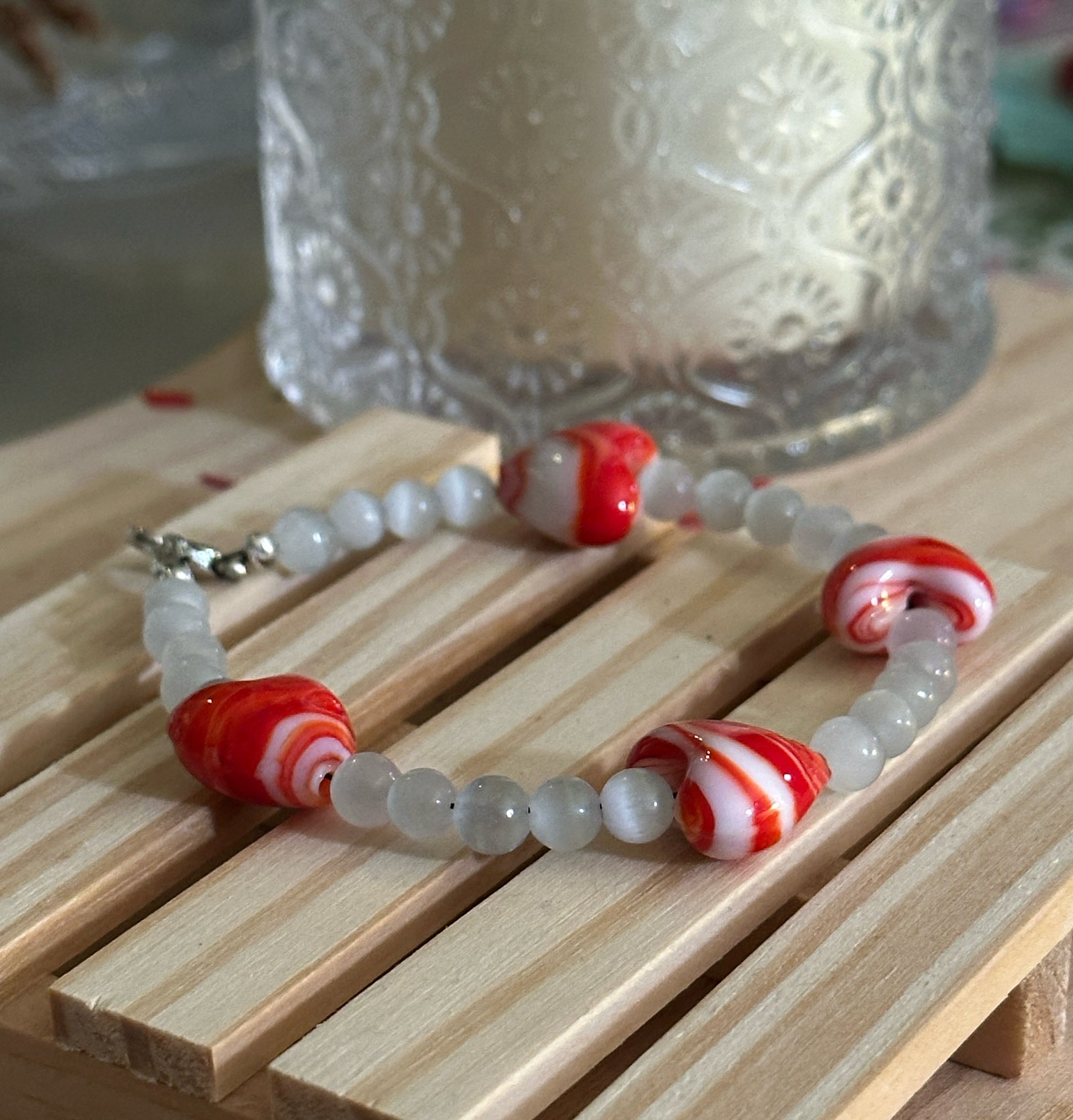 Handmade heart bead bracelet with red glass hearts styled on wood with soft candlelight background.