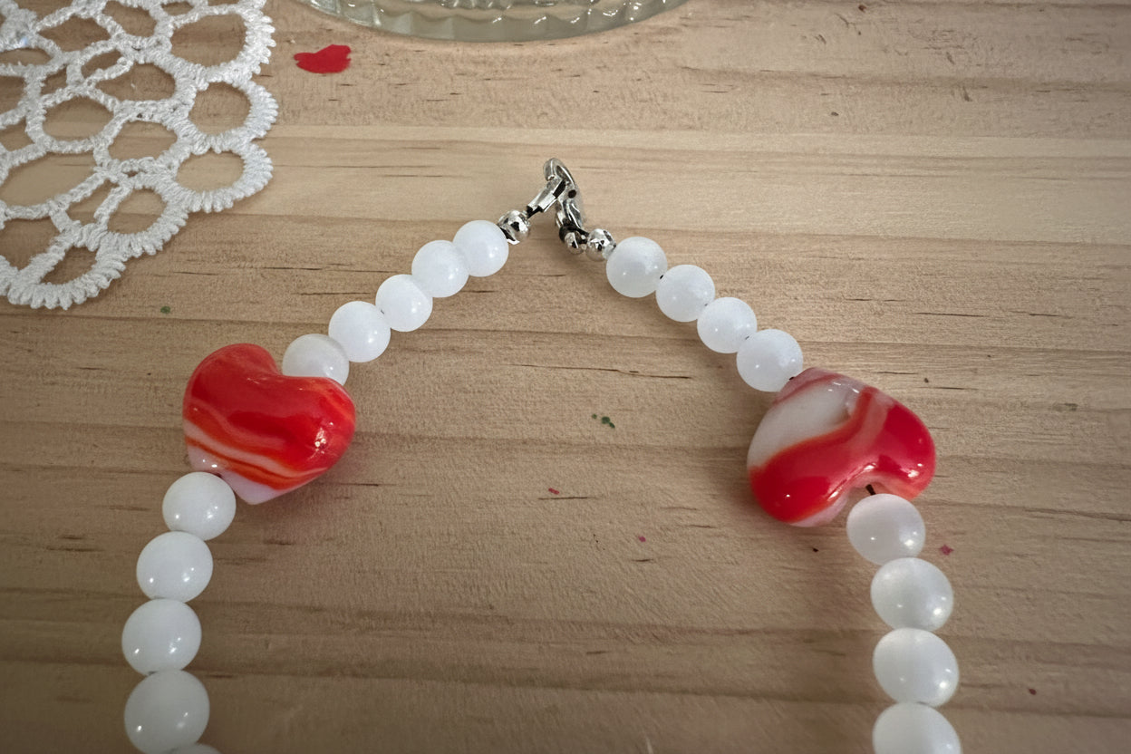 Close-up of handmade red glass heart bead bracelet showing frosted white accent beads and silver clasp.