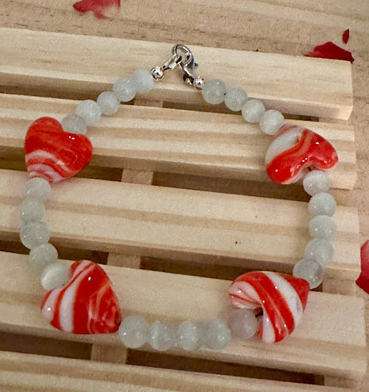 Handmade red and white glass heart bead bracelet for women displayed on wooden background, romantic love gift jewelry.
