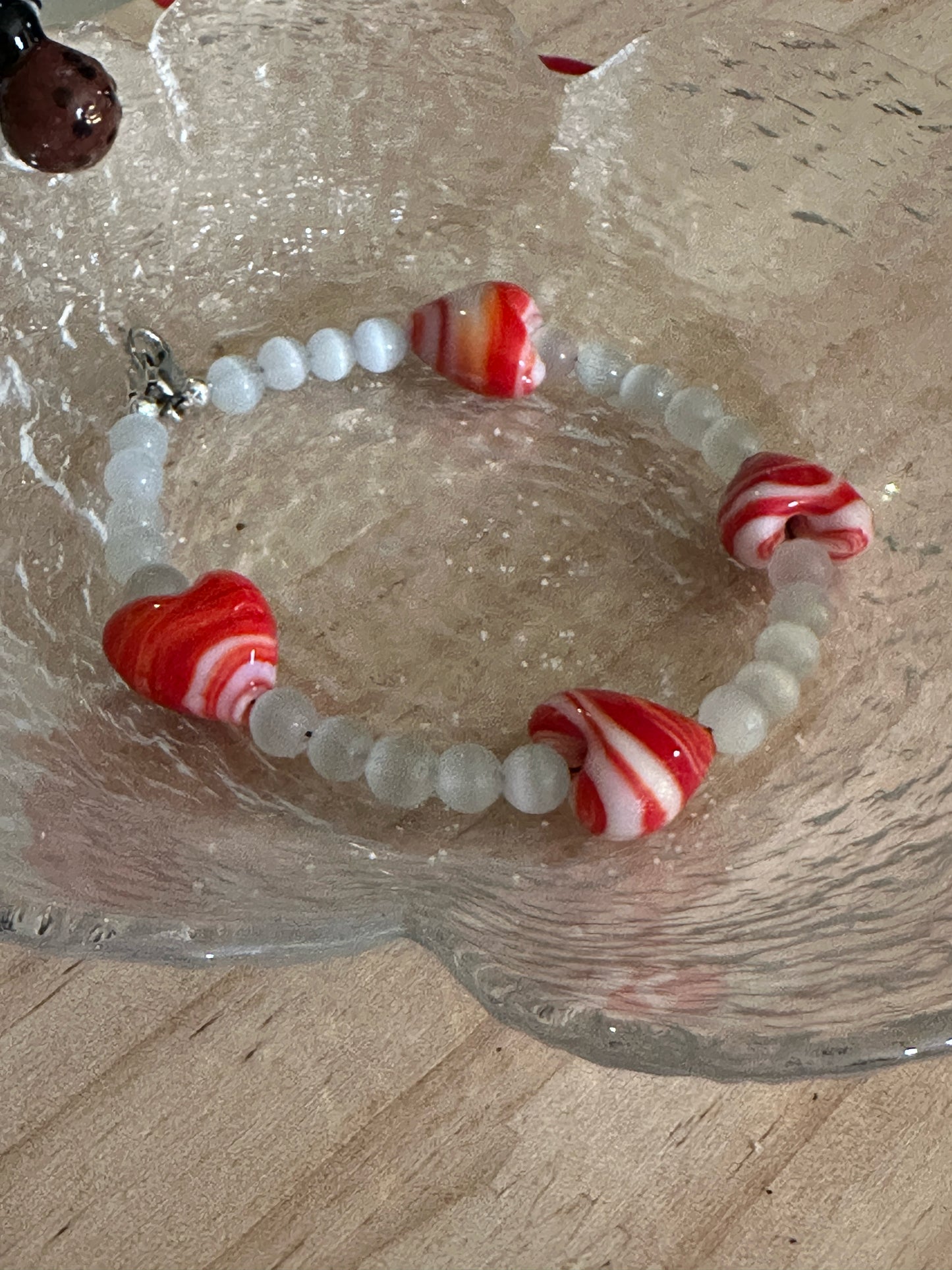 Red and white swirled glass heart bracelet arranged in textured glass dish, meaningful love jewelry gift.