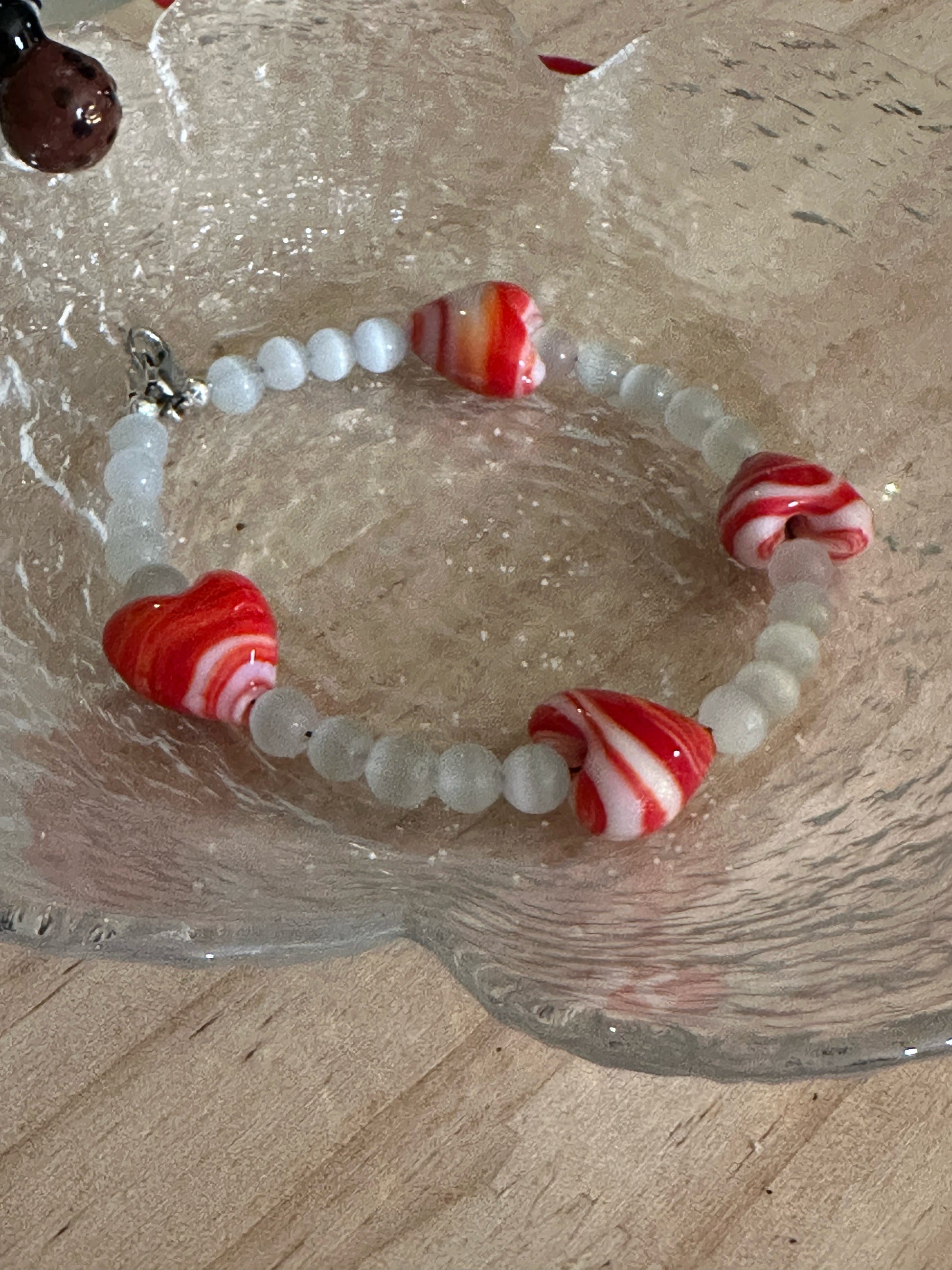 Red and white swirled glass heart bracelet arranged in textured glass dish, meaningful love jewelry gift.
