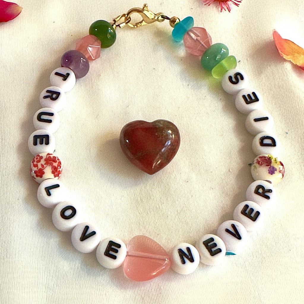 True Love Never Dies bracelet displayed beside a polished red heart stone, symbolizing enduring love, remembrance, and connection.